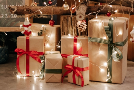 Holiday presents wrapped in brown paper and with green or red ribbon, lights strung around and above the gifts